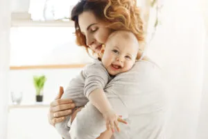 Happy Young Mom Holds Precious Little Child Gently Hugging His Little Body Kid Laughing Joyfully Looking Camera With Big Grey Eyes